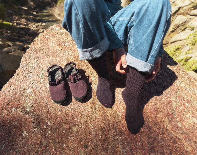 Person wearing purple shoes and socks sitting on a rock with a natural background