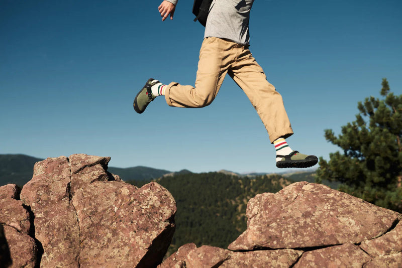 Person hiking on rocky terrain with a clear blue sky and green trees in the background