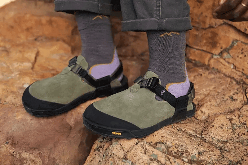 Person wearing green hiking shoes with black soles on a rocky surface