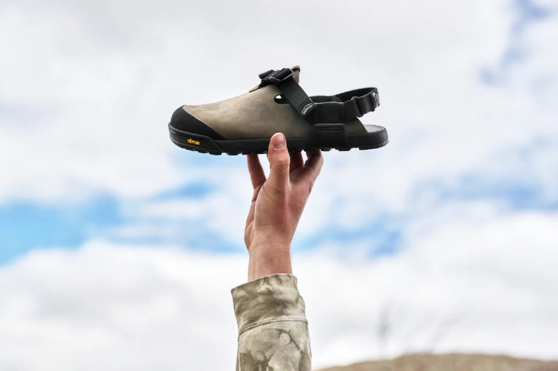 Person holding a black and brown shoe against a cloudy sky