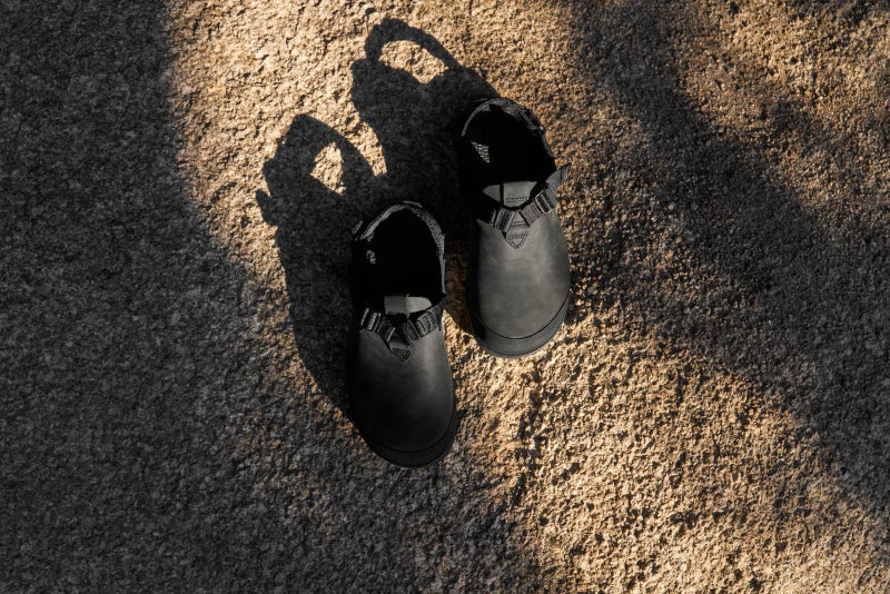 Pair of black shoes on a textured surface with shadows.