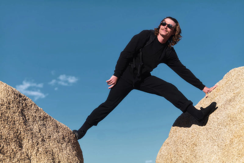 Person balancing on two large rocks wearing obsidian black mountain clogs against a clear blue sky