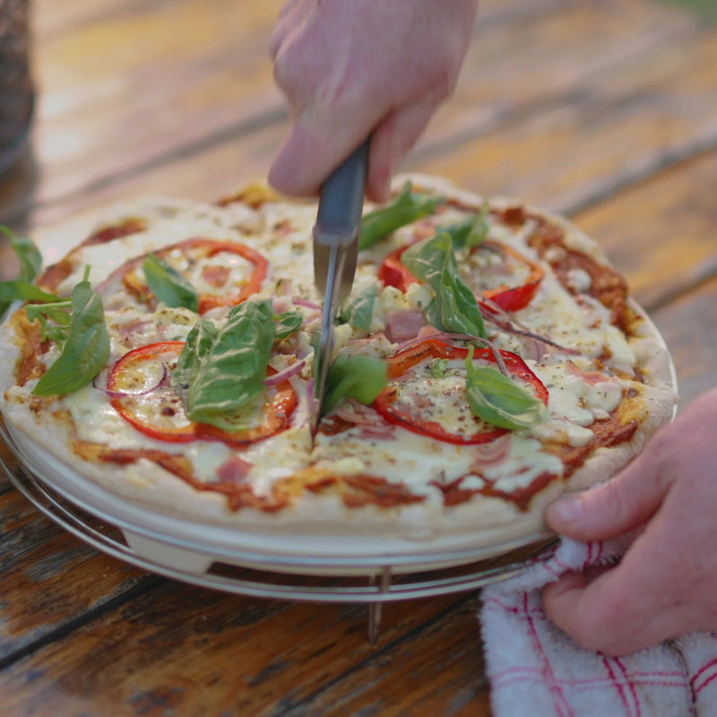 Person cutting a pizza with a fork and knife on a wooden table