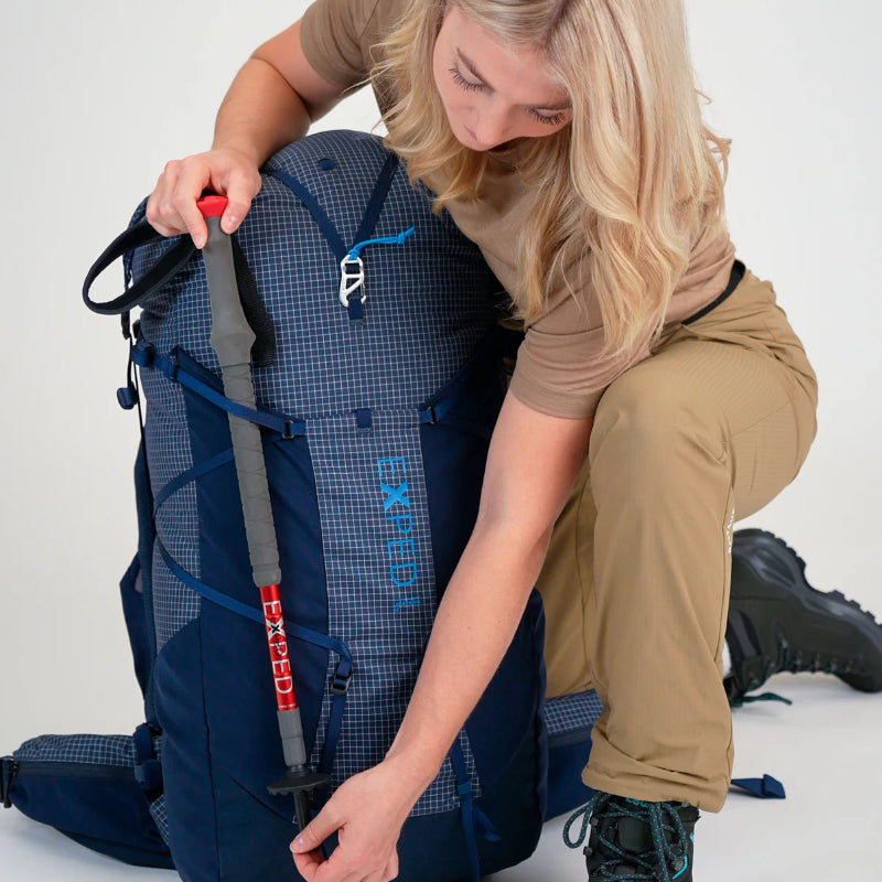 Person adjusting a blue backpack with visible branding on a white background