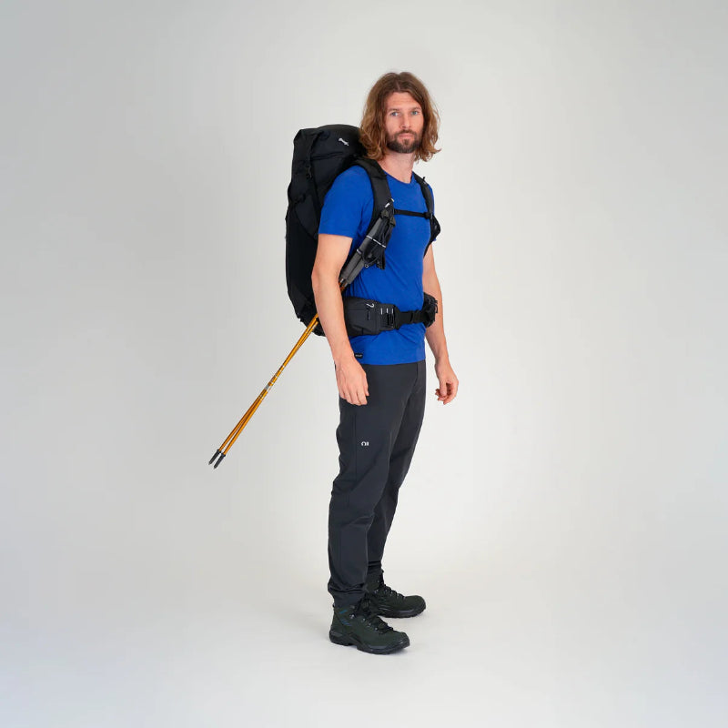 Man wearing a large black backpack and holding hiking poles on a white background