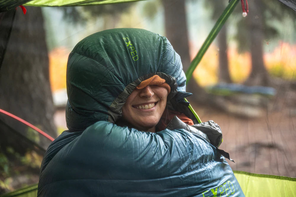 woman wrapped in a lightweight sleeping bag hiking with a forest background