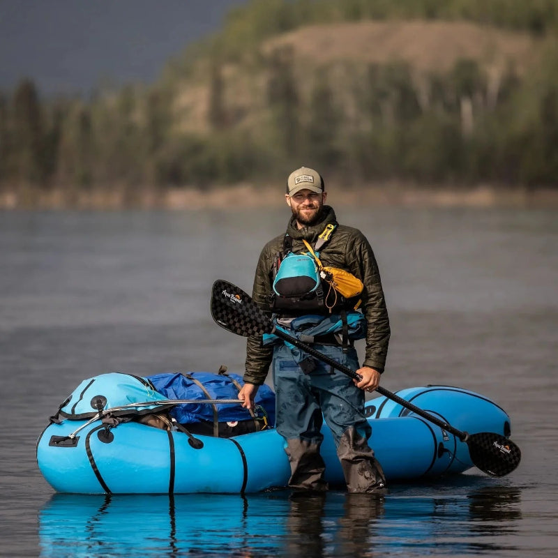 Man standing with a blue inflatable raft and paddle on a calm lake