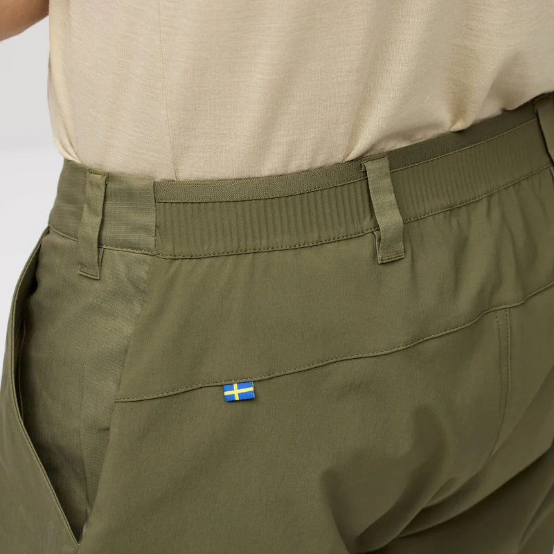 Close-up of green pants with a small flag label on a plain background