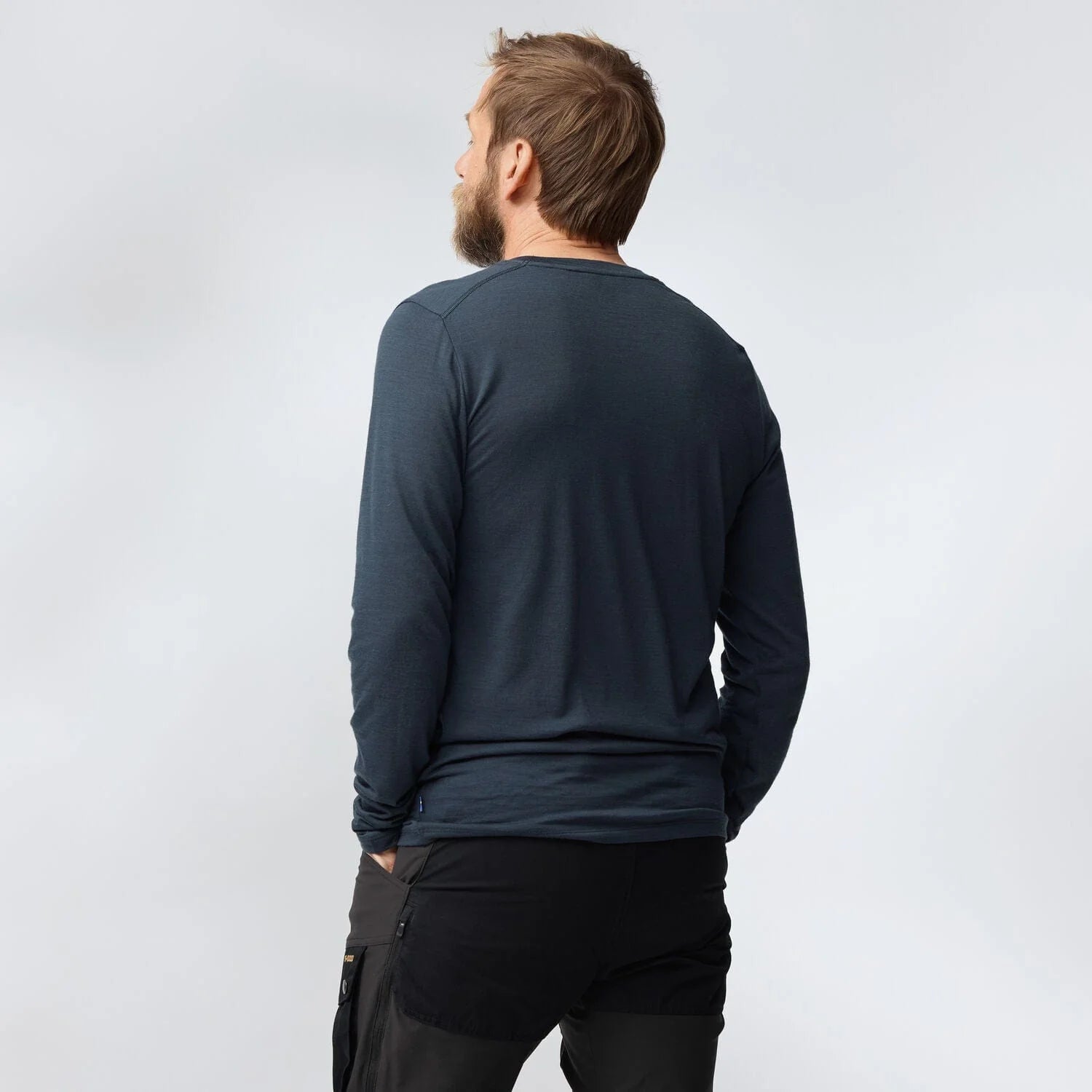 Man wearing a dark long-sleeve shirt and black pants on a light gray background