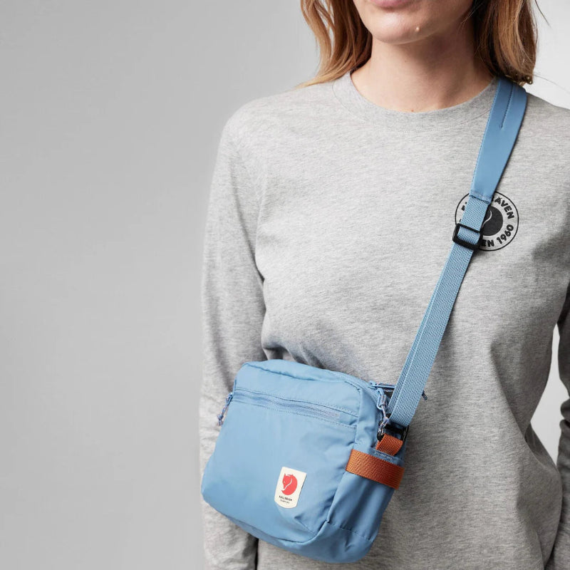 Person wearing a blue crossbody bag with a gray background