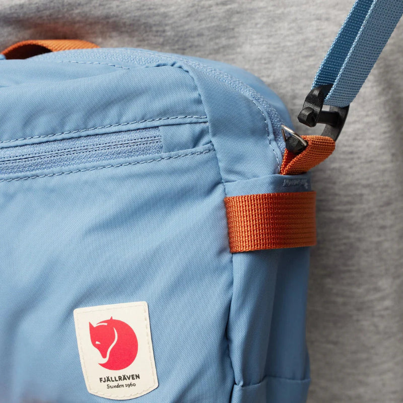 Close-up of a blue bag with an orange strap and Fjällräven logo on a gray background