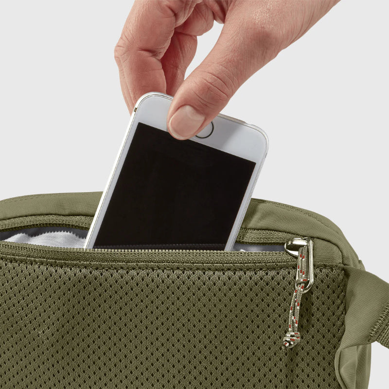 Hand placing a smartphone into a green bag on a light gray background