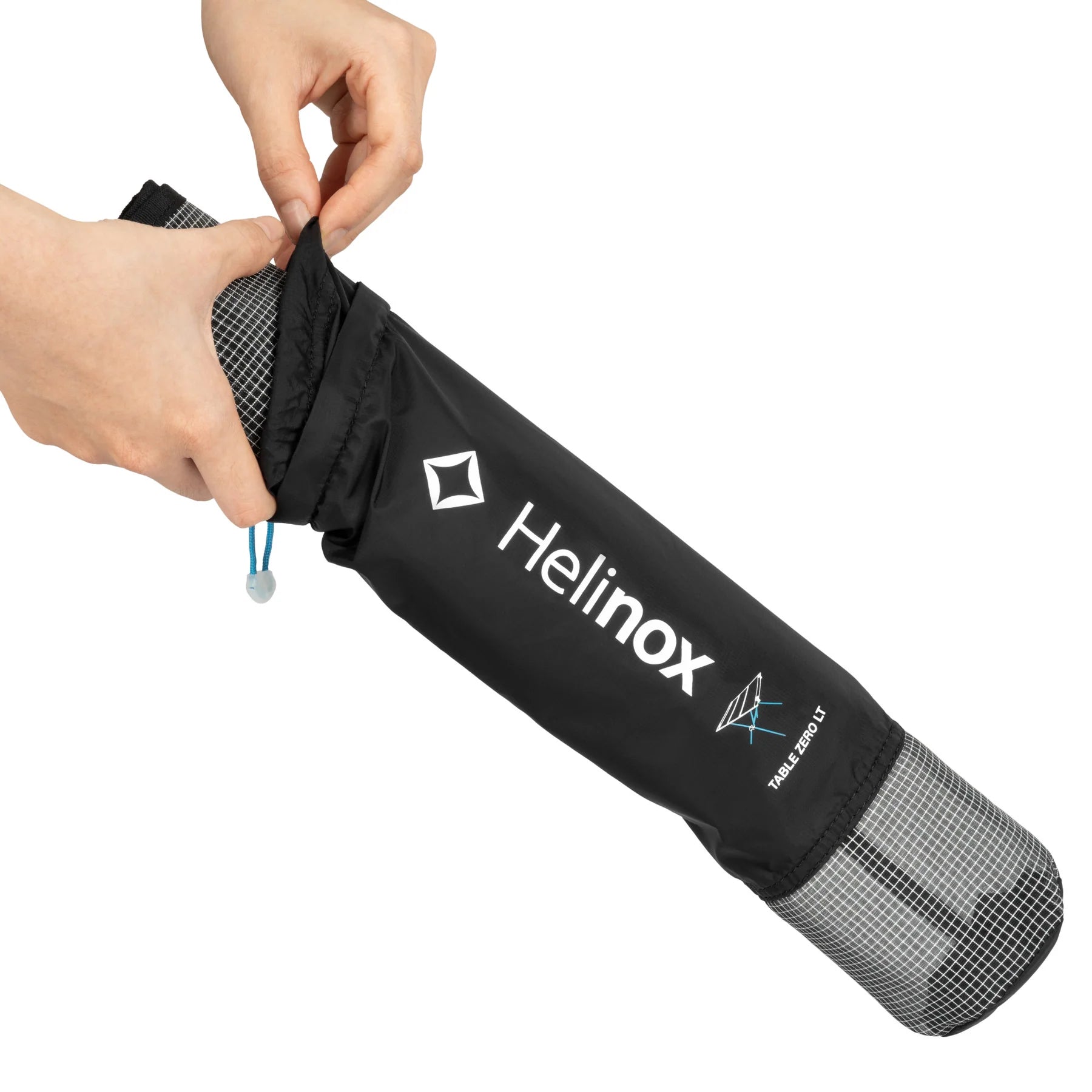 Black Helinox camping table being placed into a Helinox bag open on a white background