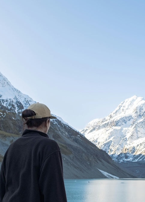 female hiker standing by a lake with snow-capped mountains in the background in New Zealand South Island