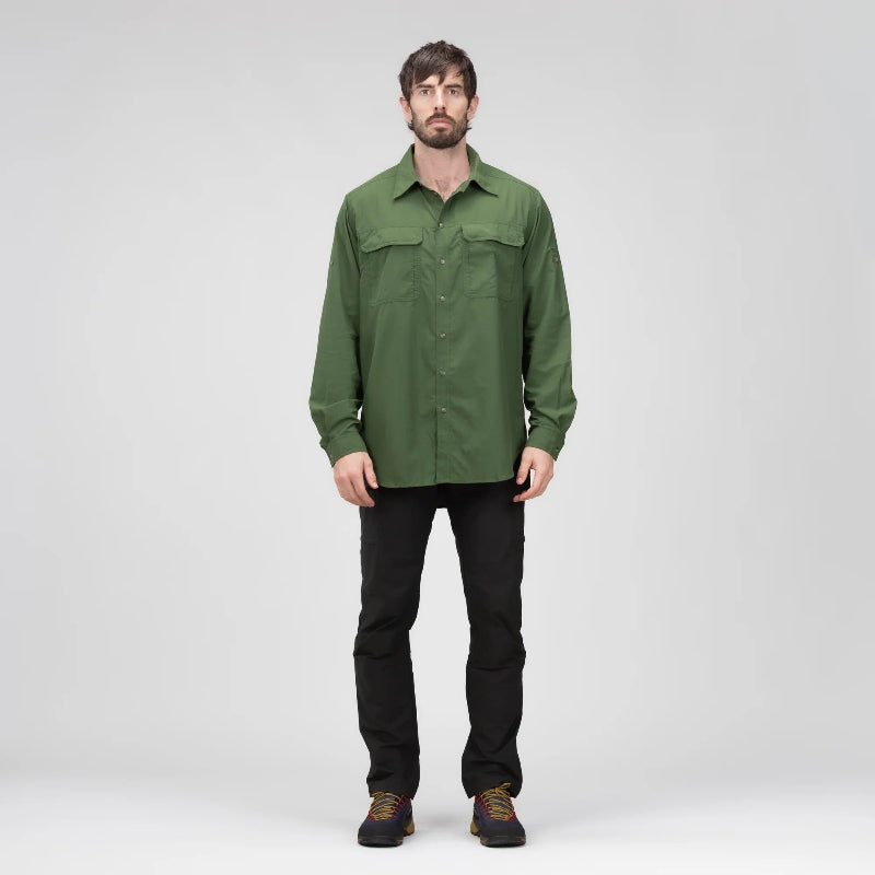 A man wearing an olive green long-sleeve button-up shirt, black pants, and brown shoes, standing against a light gray studio background.