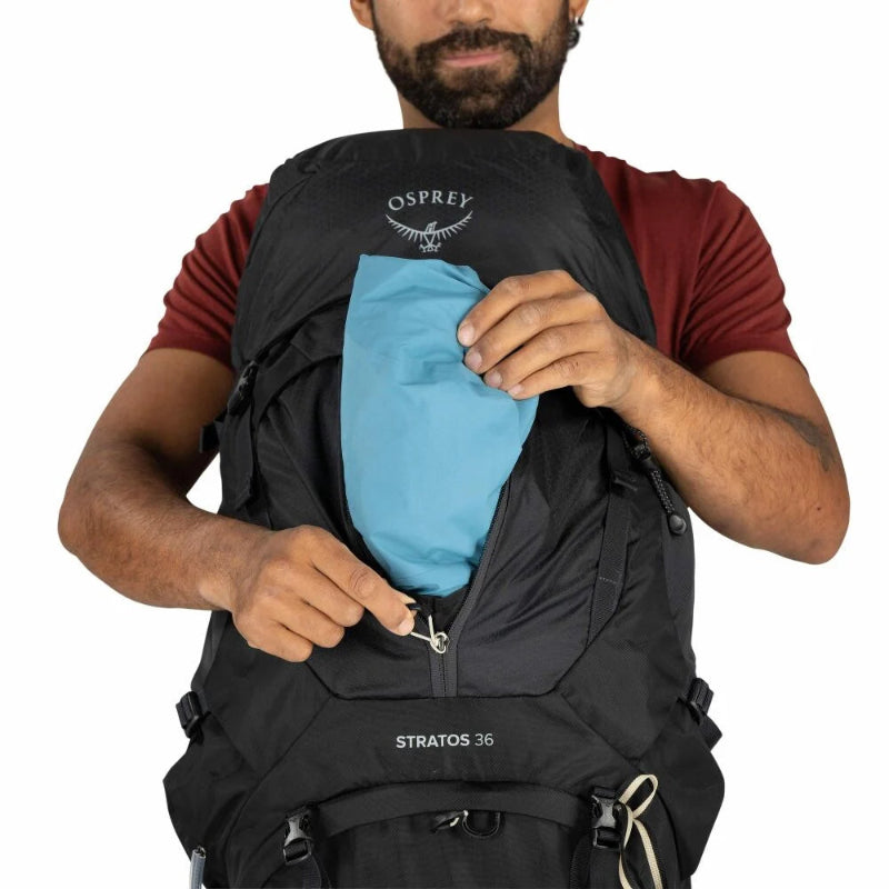 Person holding a black Osprey Stratos 36 backpack with a blue compartment.