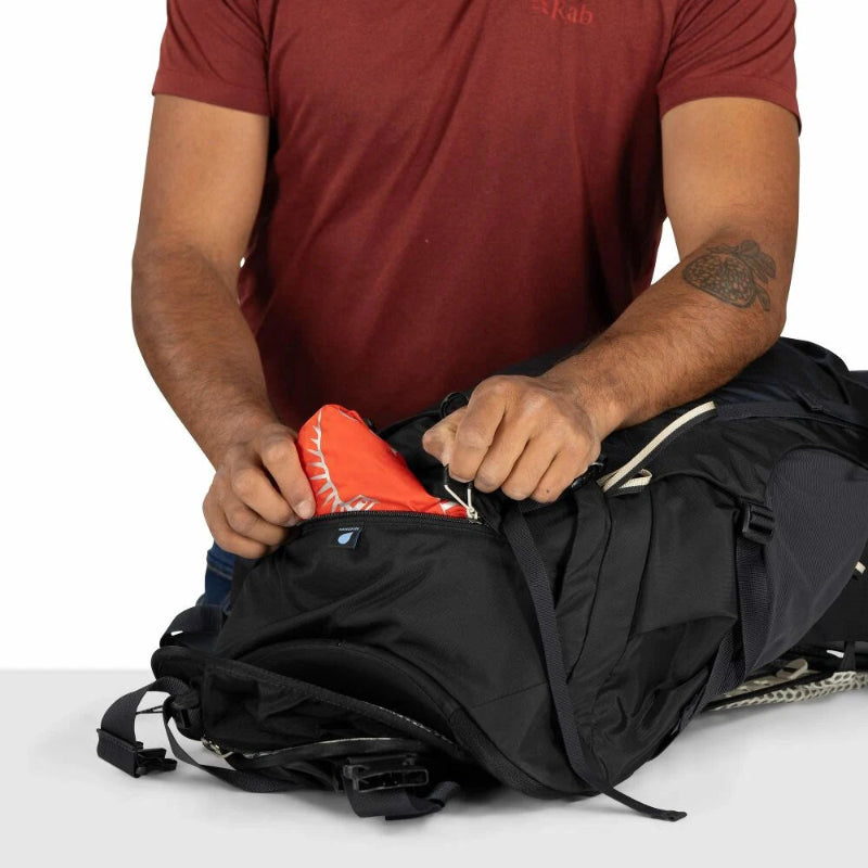 Person packing an orange raincover into a black backpack on a white background
