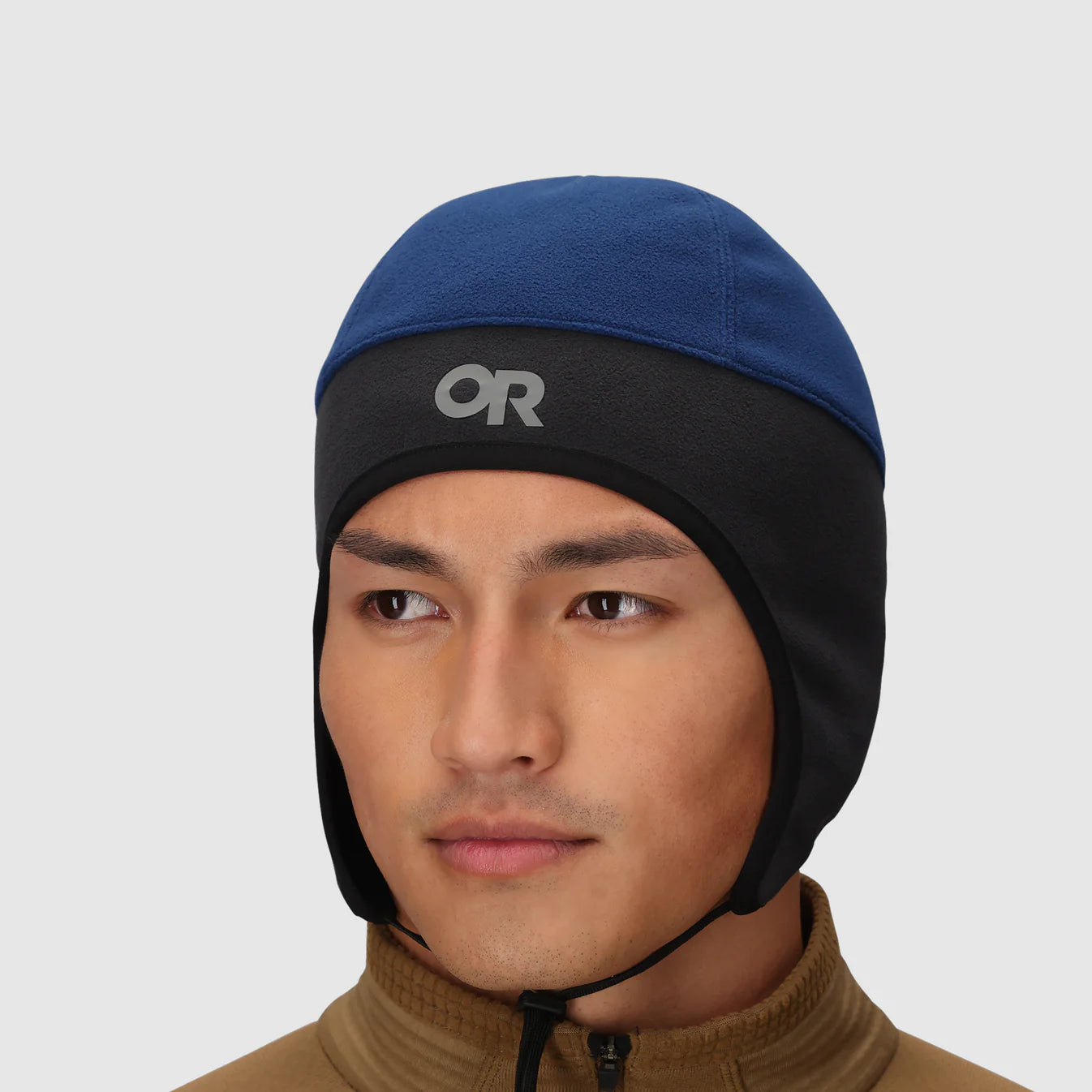 Man wearing a blue and black beanie with a brand logo on a light gray background