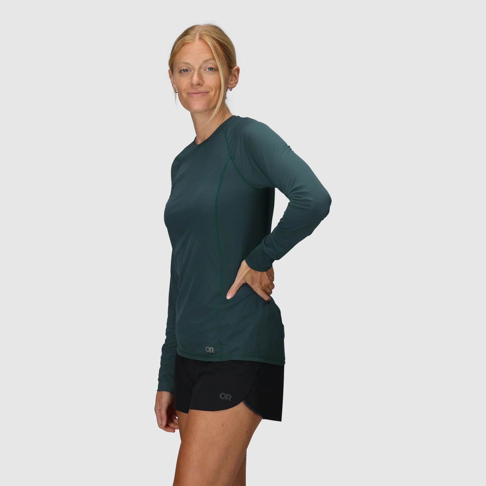 Woman wearing a green long-sleeve hiking top and black womens trekking shorts on a white background