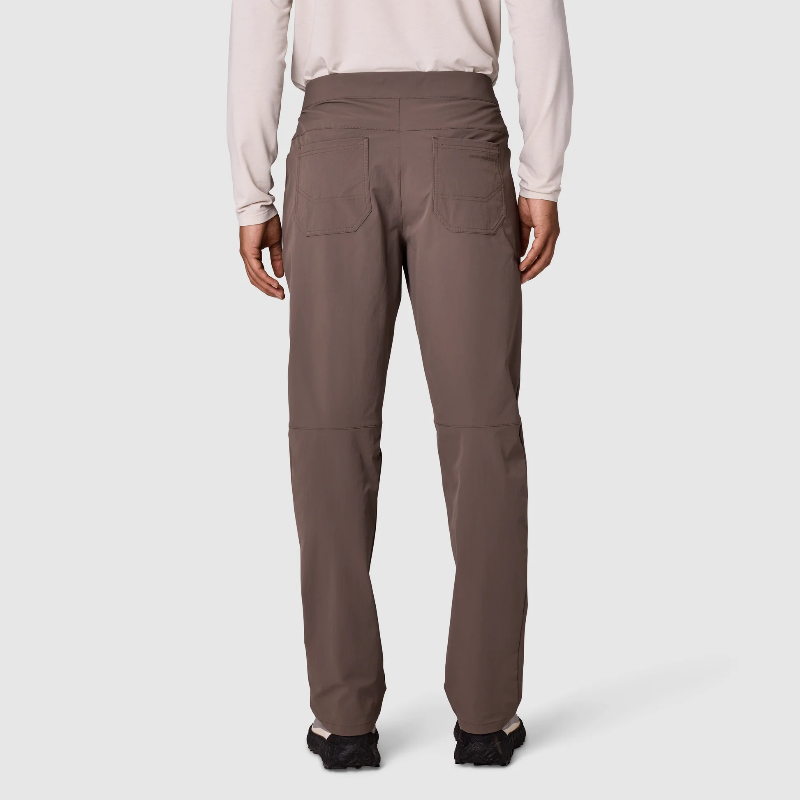 Rear view of a person wearing brown utility pants with a light beige long-sleeve top and black shoes, photographed against a light gray studio background.