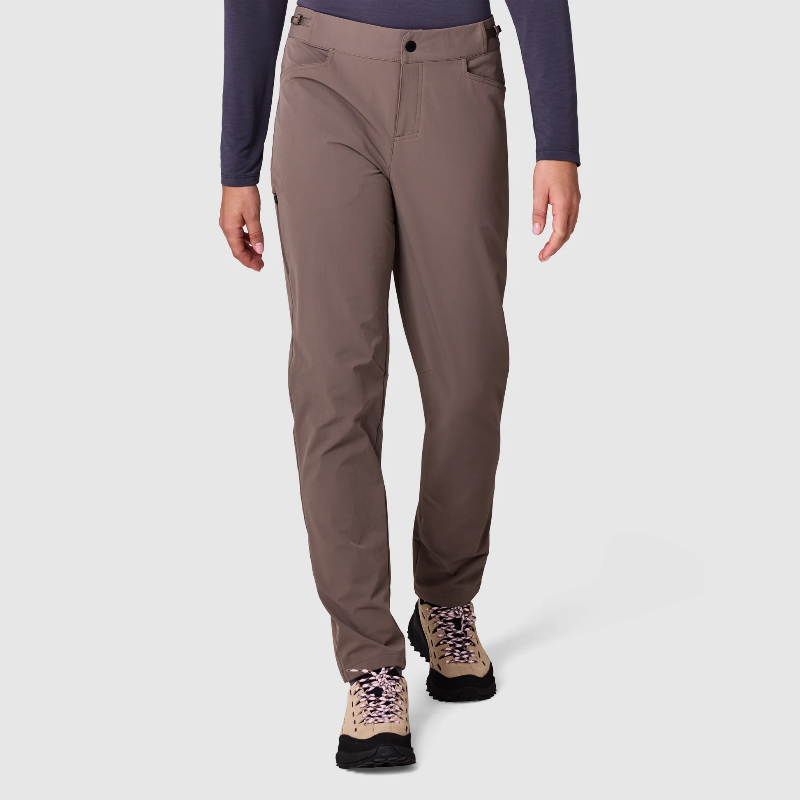 A person wearing slim-fit brown hiking pants, a dark purple long-sleeve top, and hiking boots, shown from the waist down against a light gray studio background.