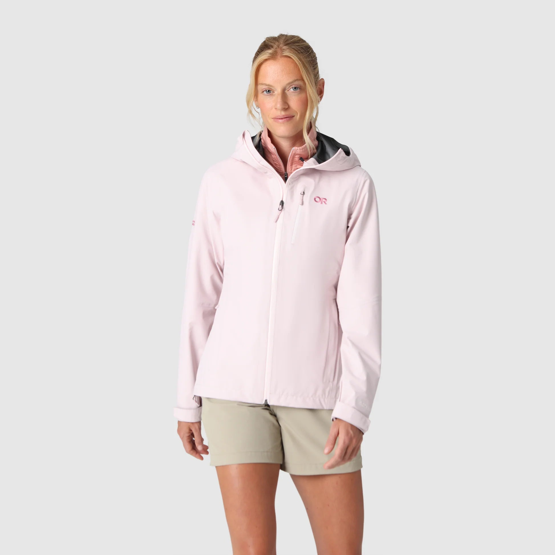 Woman wearing a light pink rain jacket on a gray background