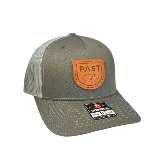 A green PAST Outdoors trucker's hat with an orange brand patch on the front, featuring a pre-curved visor and an adjustable snapback.