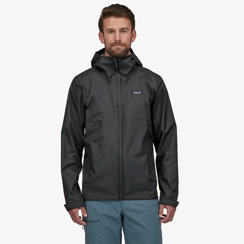Man wearing the black Patagonia Men's Torrentshell 3L Rain Jacket with blue pants