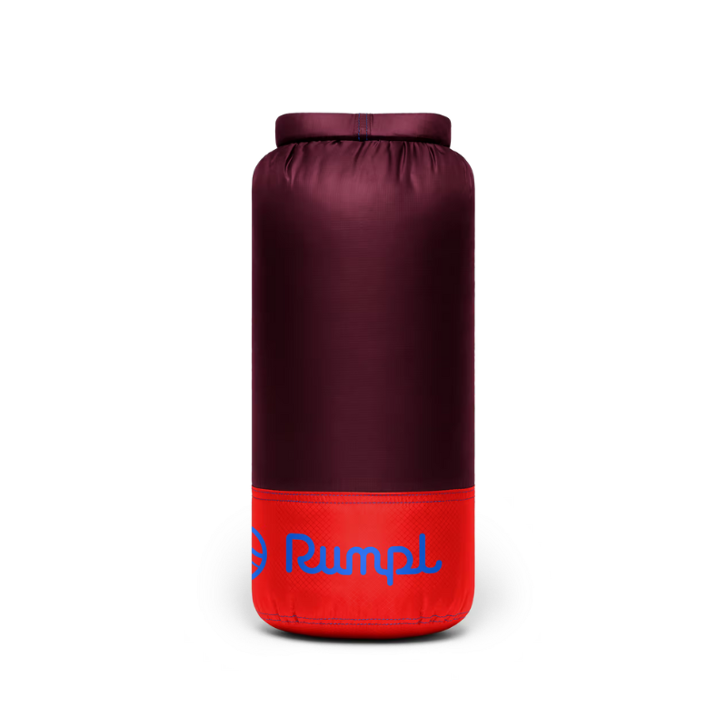 A cylindrical camping sleeping bag or insulated bag shown upright on a plain white background. The upper portion is a dark burgundy/plum color, and the lower portion is bright red with a blue 'Rumal' logo printed on it.