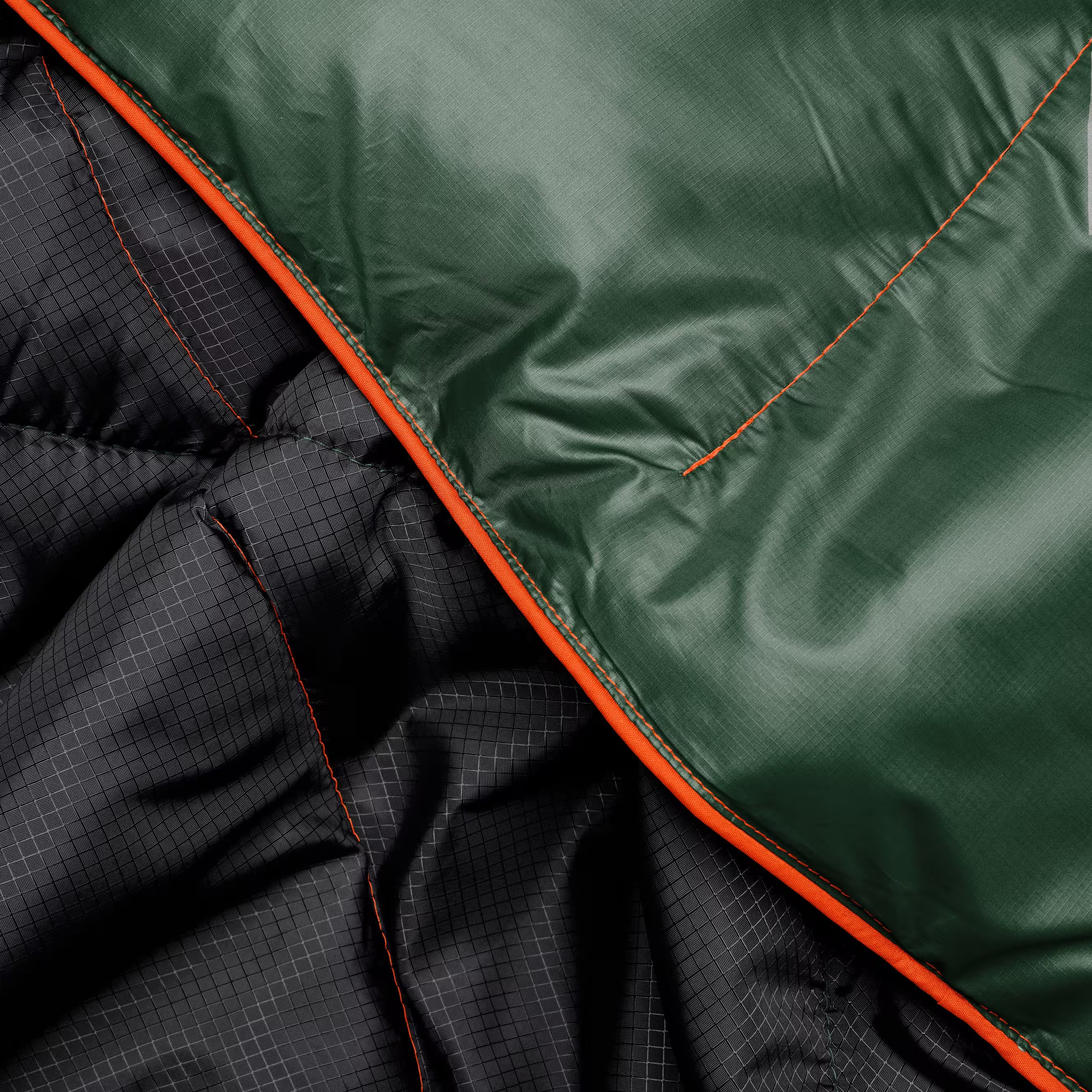 Close-up of a puffer jacket showing a dark green waterproof shell, a black patterned quilted interior, and bright orange piping trim.