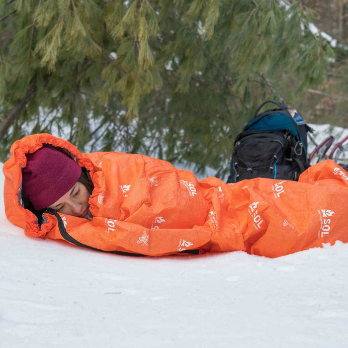 Person sleeping in a n orange SOL Escape Bivvy in a snowy forest