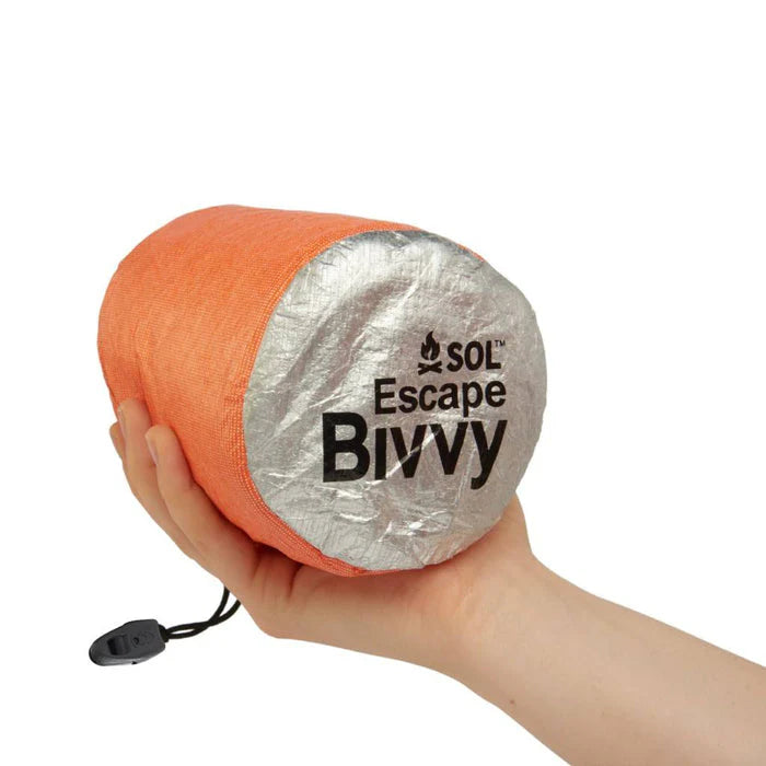 Hand holding a rolled-up orange and silver SOL Escape Bivvy against a white background