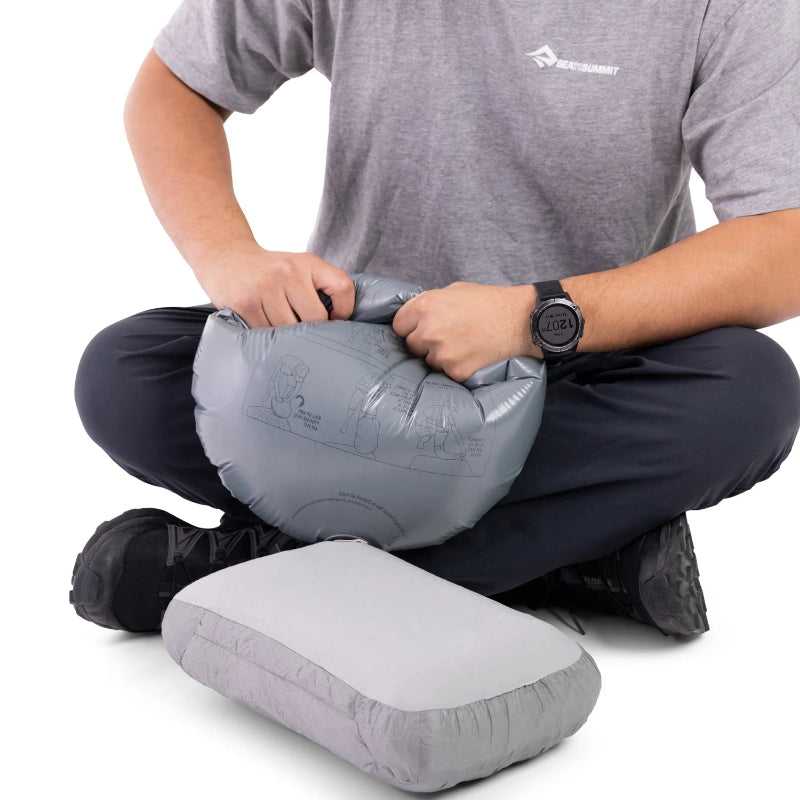 Person inflating a gray inflatable pillow with a visible brand logo on a white background