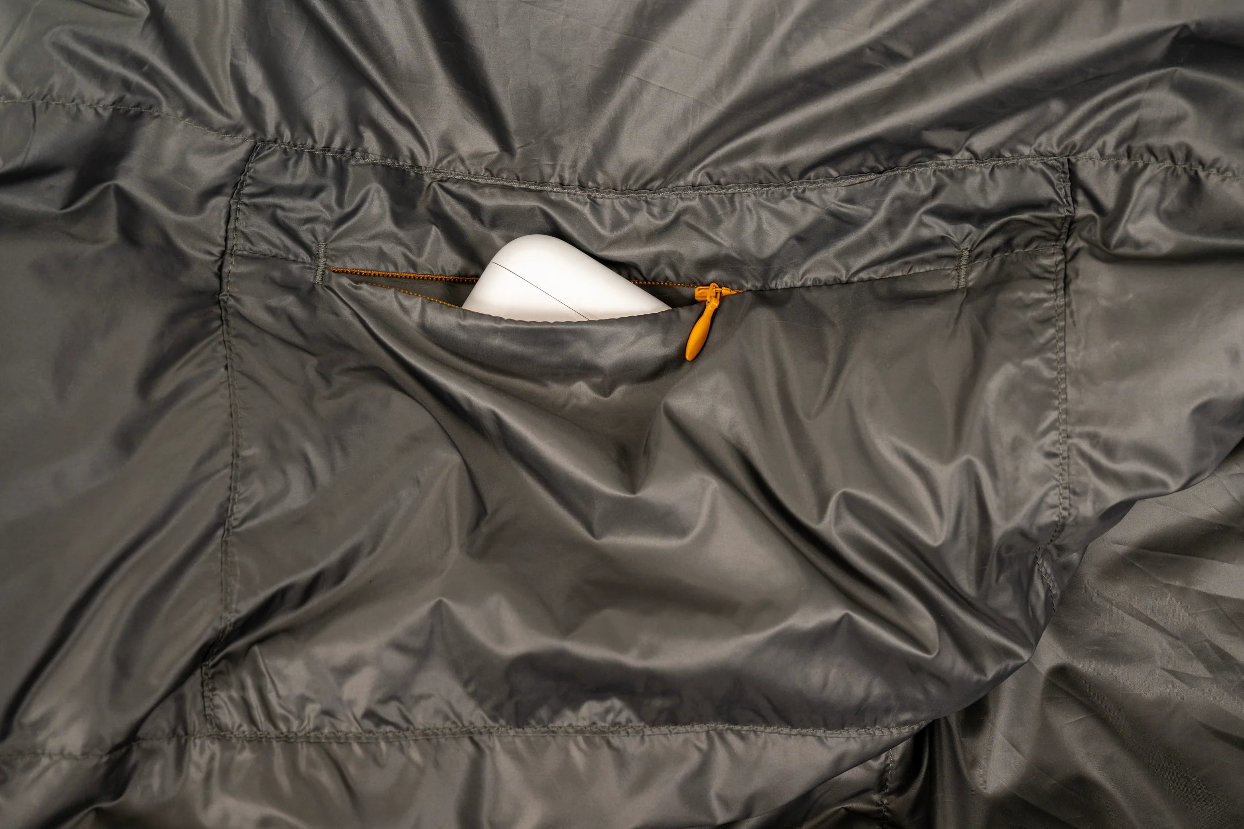 Close-up of a gray lightweight sleeping bag for hiking with a zipper pocket, showing a white object inside.