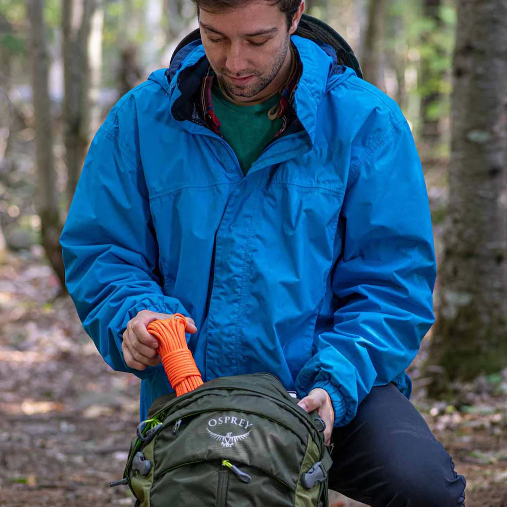 Person in a blue jacket with an Osprey backpack in a forest setting pulling tinder cord 