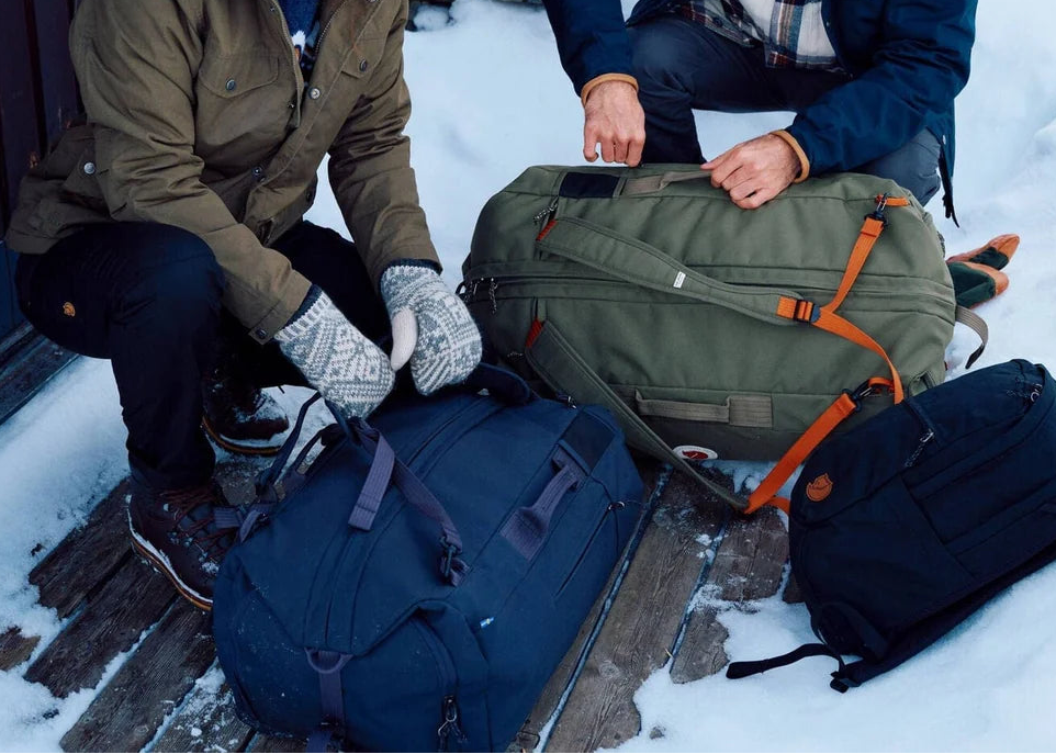 Two people preparing their luggage in the snow with duffle bags