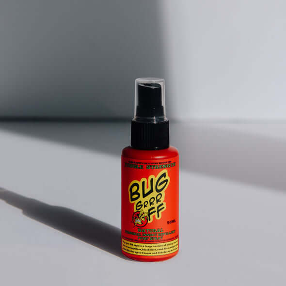 A red spray bottle labeled 'Bug Grrr Off' on a shadowy background, indicating a natural insect repellent.