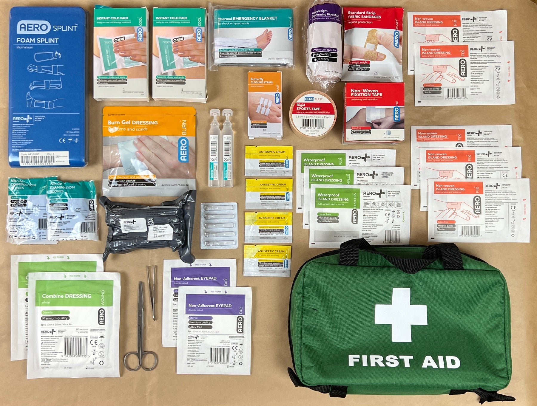 Contents of a first aid kit displayed on a table, including various bandages, antiseptic wipes, eye pads, gloves, scissors, and a green first aid bag.